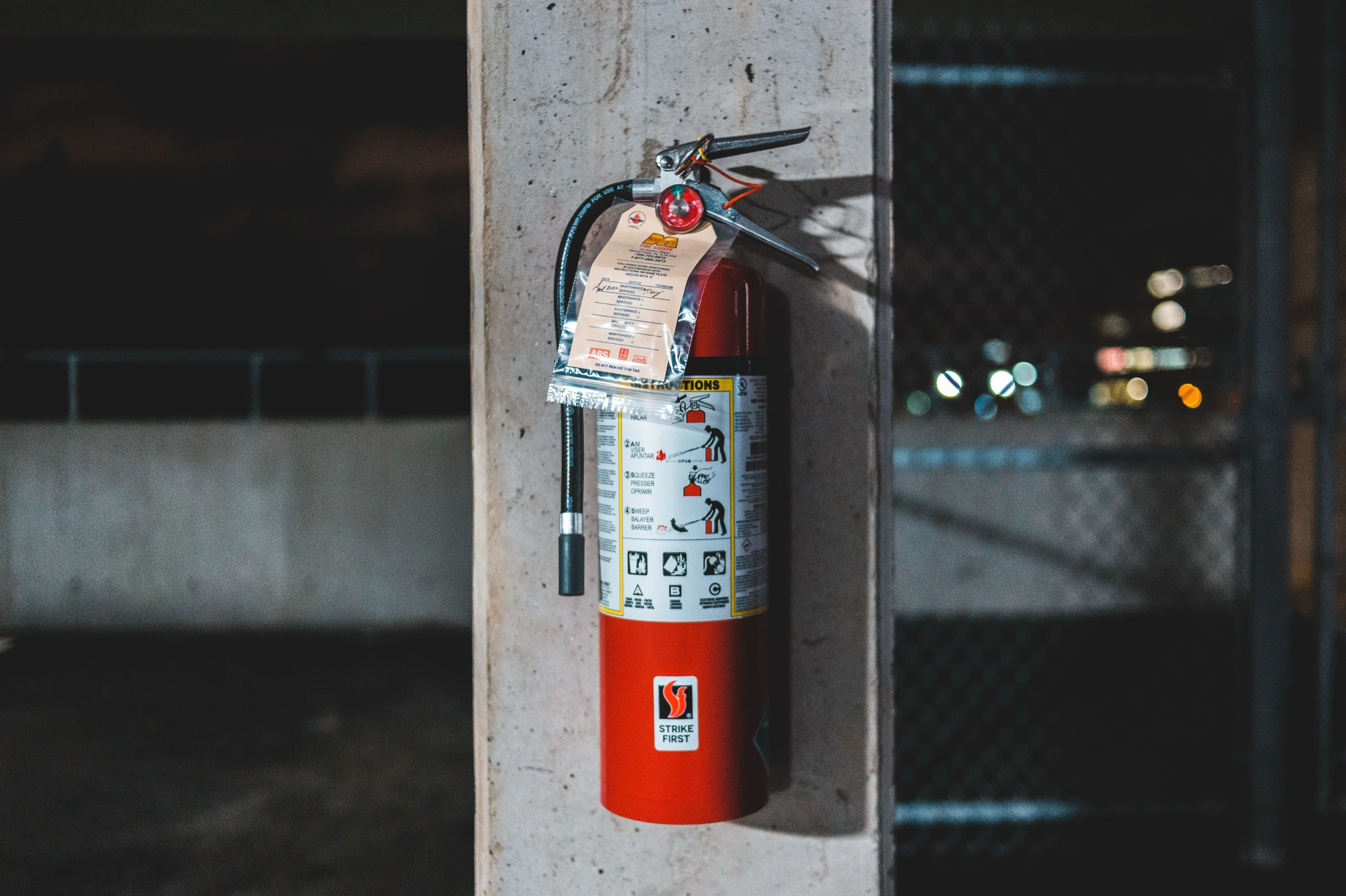 A red fire extinguisher on a concrete pillar with a signed maintenance tag hanging from it